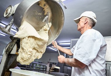 Profesyonel erkek Baker hamur ile profesyonel yoğurucu makinesini karıştırıyor. Un ürünleri yapmak için ekipman