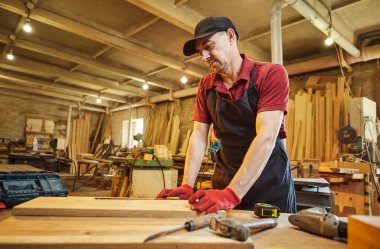 Marangoz bir ahşap ile çalışır, bir kalemle tahta işaretler ve bir marangoz atölyesinde mobilya yapmak için bir parça odun kesmek için ölçümler alır.