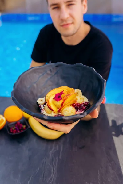 Cheerful man eat sweet oatmeal with fried cheese balls, peach and cranberries. Healthy breakfast