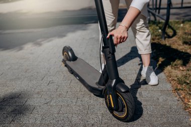 Close up of woman in white suit folding her electro scooter after ride while standing in city parkland