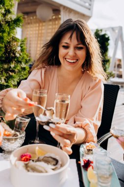 Beautiful Woman eating fresh oysters and drinking chilled prosecco wine on the summer sunset in restaurant. Seafood delicacies