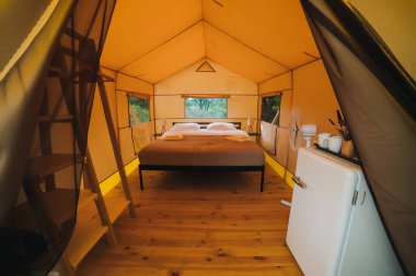 Interior of Cozy open glamping tent with light inside during dusk. Luxury camping tent for outdoor summer holiday and vacation. Lifestyle concept