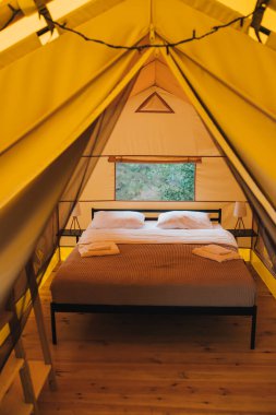Interior of Cozy open glamping tent with light inside during dusk. Luxury camping tent for outdoor summer holiday and vacation. Lifestyle concept