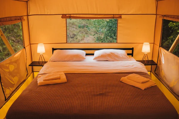 Interior of Cozy open glamping tent with light inside during dusk. Luxury camping tent for outdoor summer holiday and vacation. Lifestyle concept