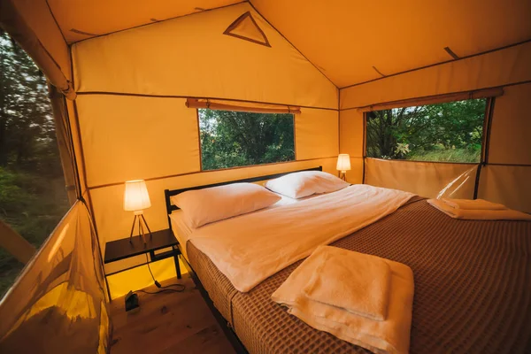 Interior of Cozy open glamping tent with light inside during dusk. Luxury camping tent for outdoor summer holiday and vacation. Lifestyle concept