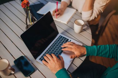 Close up of Woman freelancer making notes while male colleague working laptop sitting in cozy glamping tent in summer evening