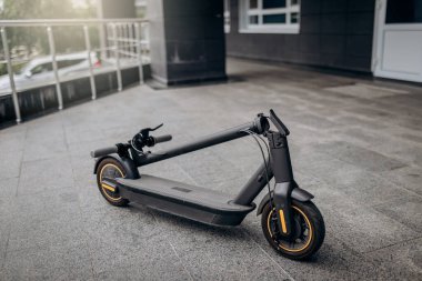 Folded Electric scooter on concrete surface on urban street near modern building