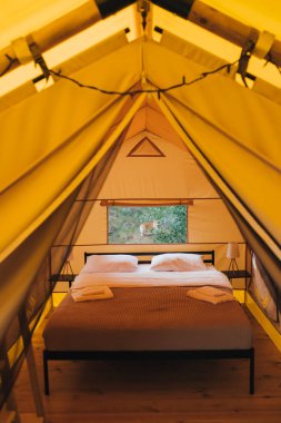 Interior of Cozy open glamping tent with light inside during dusk. Luxury camping tent for outdoor summer holiday and vacation. Lifestyle concept