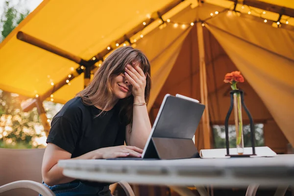 Tired Woman freelancer  using a laptop on a cozy glamping tent in a sunny day. Luxury camping tent for outdoor summer holiday and vacation. Lifestyle concept