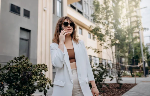 Smiling Businesswoman White Suit Talking Phone Walking City Modern Architecture — Φωτογραφία Αρχείου