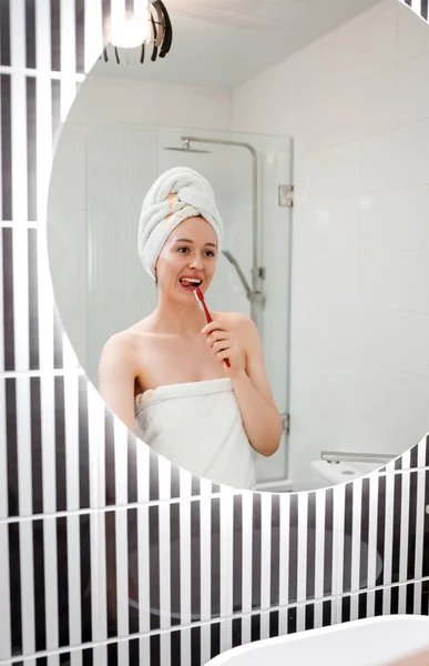 浴室の鏡の前に白いタオルで歯を磨く美しい若い女性の肖像画 朝のルーチンの美しさ手順 — ストック写真