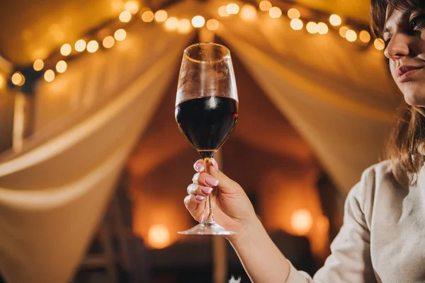 Close up of Woman freelancer drinking wine sitting in cozy glamping tent in autumn evening. Luxury camping tent for outdoor holiday and vacation. Lifestyle concept