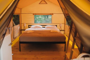Interior of Cozy open glamping tent with light inside during dusk. Luxury camping tent for outdoor summer holiday and vacation. Lifestyle concept