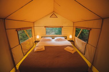 Interior of Cozy open glamping tent with light inside during dusk. Luxury camping tent for outdoor summer holiday and vacation. Lifestyle concept