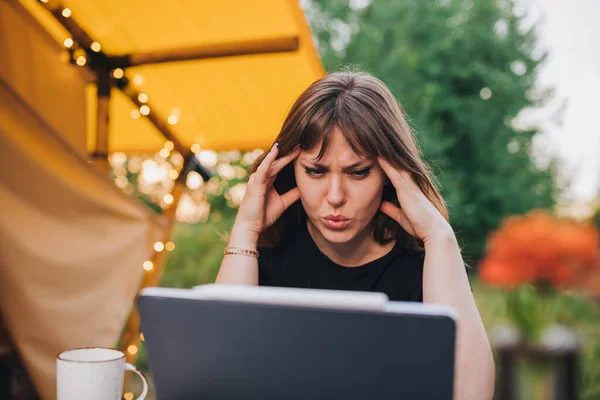 Tired Woman freelancer using a laptop on a cozy glamping tent in a sunny day. Luxury camping tent for outdoor summer holiday and vacation. Lifestyle concept