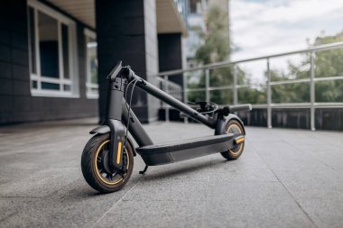 Folded Electric scooter on concrete surface on urban street near modern building
