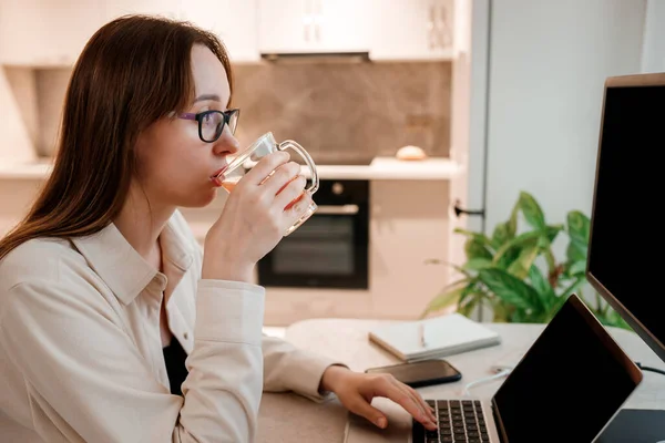 Businesswoman working at home office on laptop and drink juice. Young happy female student studying in online university