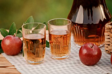 Elma suyu ve elma sepetli iki bardak, ahşap masa ve doğal meyve bahçesi arkaplanı. Vejetaryen meyve kompozisyonu