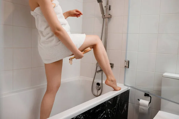 照片是一位穿着白色毛巾的年轻女子在家里的浴室里用干木刷子做身体淋巴引流按摩 反蜂窝演习 — 图库照片