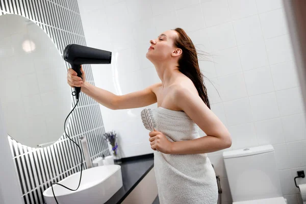 若い女性は ヘアドライヤーで髪を乾燥させ スタイリング 現代のバスルームのインテリアで髪型を作ります 朝のシャワー後の美容ルーチン — ストック写真