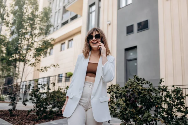 Smiling Businesswoman White Suit Talking Phone Walking City Modern Architecture — Φωτογραφία Αρχείου