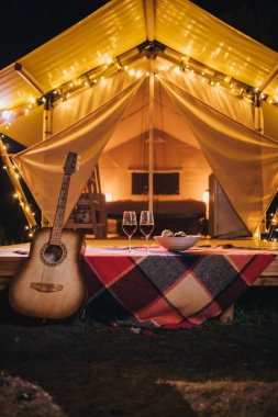 Sonbahar akşamı rahat bir çadırın arka planında duran meyveli iki kadeh kırmızı şarap ve tabak. Açık hava tatili ve tatil için lüks kamp çadırı. Yaşam tarzı kavramı   