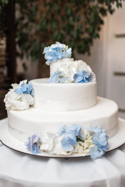Tarta de boda blanca con flores azules en una mesa —  Fotos de Stock