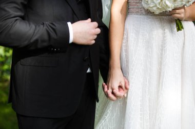 Gelin ve damat el ele tutuşuyor. Nişan yüzüğü gelinin parmağında.