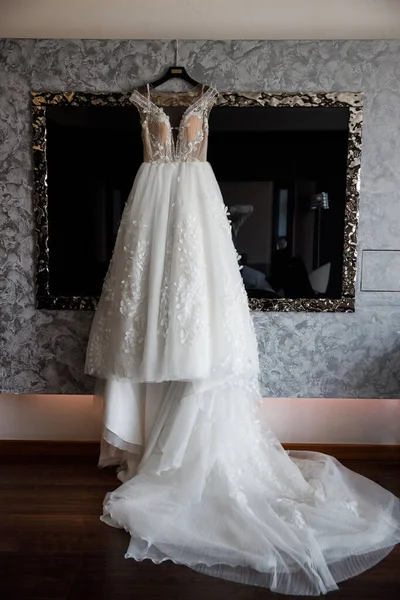 Wedding dress hanging on the mirror in the room.