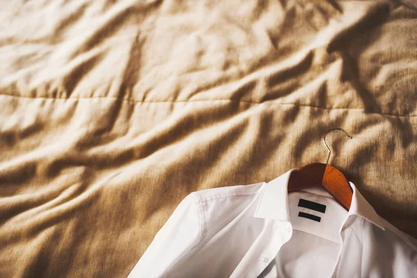 ベッドの上に木製のハンガー付きの白いウェディングシャツ — ストック写真