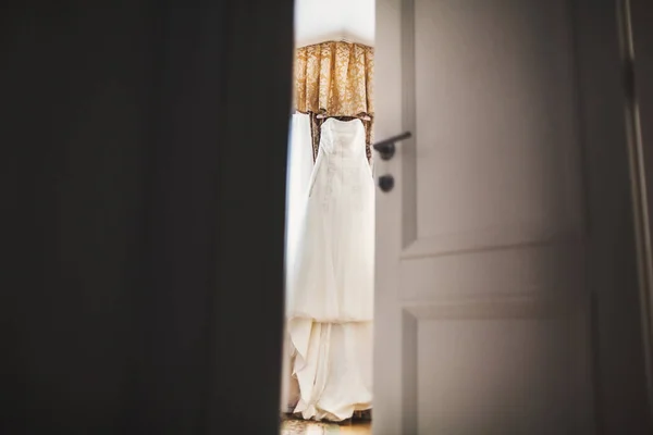Wedding dress hanging in the room near the window.