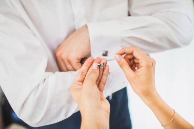 Groom in the morning during wedding preparations. Bride helping groom put on cufflinks