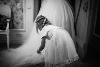 Bride in the morning during wedding preparations. The little bridesmaid helps lift the dress