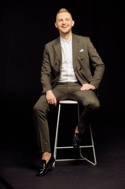 Tarz sahibi takım elbiseli, siyah renkli stüdyo arka planında izole edilmiş gülümseyen meraklı bir adamın fotoğrafı.