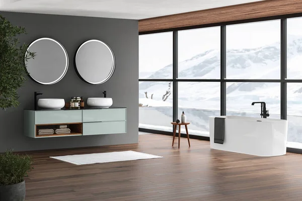 Modern bathroom interior with dark brown parquet floor, white oval bathtub and two sinks, side view. Minimalist bathroom with modern furniture , pool and snowy mountain view from window. 3D rendering