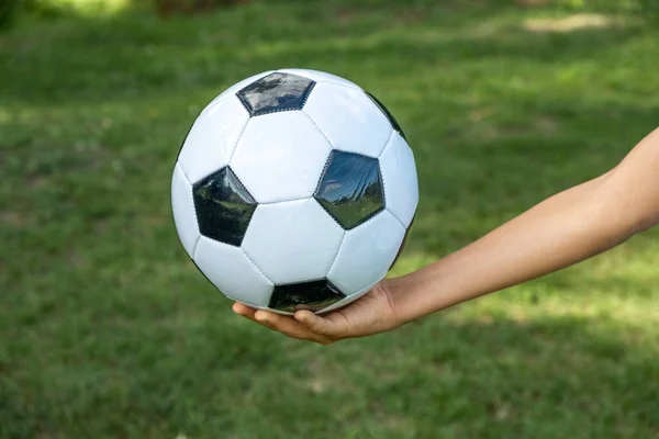 Fußball weißes und schwarzes Leder in der Hand eines Fußballers auf grünem Rasen. — Stockfoto