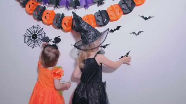 4k. Dvě holčičky děti v karnevalových kostýmech se připravují na Halloween zdobení stěny v pokoji černými netopýry. — Stock video