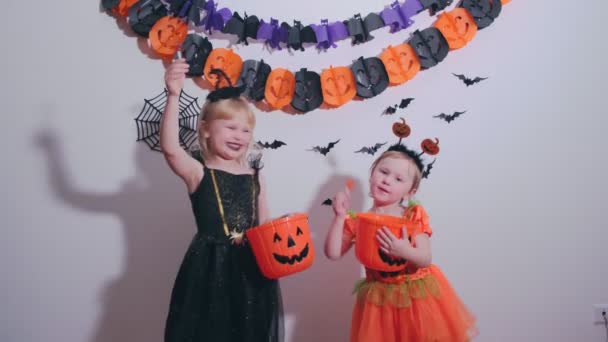Małe ślicznotki w kostiumie Halloween jedzące lizaki w domu na imprezie Hallowen. — Wideo stockowe