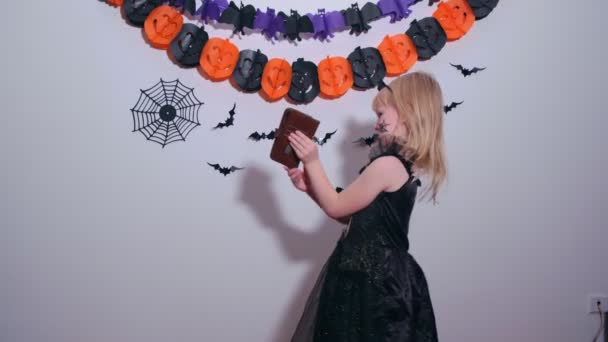 Malá dívka v kostýmu čarodějnice používá mobilní telefon k videohovory a ukázat halloween dekor doma — Stock video