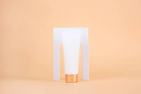 Mockup tubo crema blanca en podio blanco con arco sobre fondo beige. — Foto de Stock