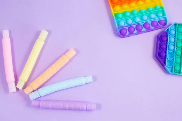Tubo corrugado plástico brillante multicolor y pop-it sobre fondo púrpura. — Foto de Stock