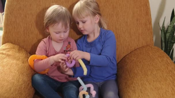 Twee kleine meisjes zitten in een stoel en spelen met anti-stress — Stockvideo
