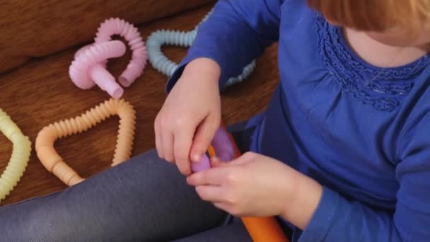 Mãos de criança brincando com anti-stress Brinquedos de tubo pop sentados em um sofá . — Vídeo de Stock