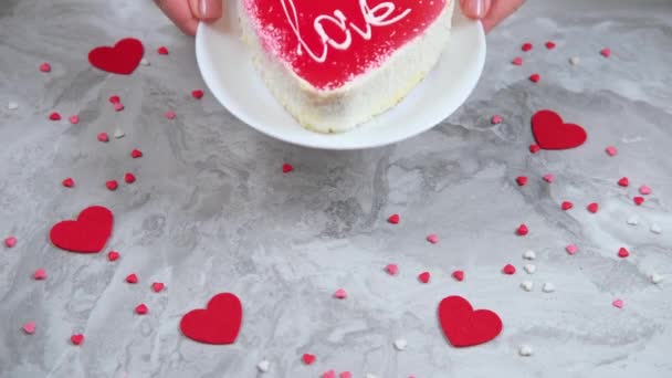 Frauenhände legen einen leckeren roten herzförmigen Kuchen auf einen dekorierten Marmortisch. — Stockvideo