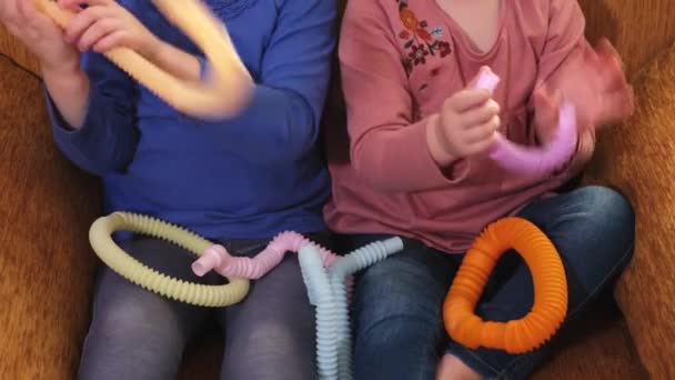 Dos niñas pequeñas mano jugando con el tubo anti estrés Pop sentado en una silla. — Vídeo de stock