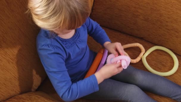 Дитячі руки грають з антистресовими іграшками поп-трубки, що сидять в дивані  . — стокове відео