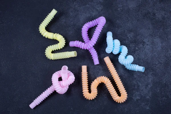 Tubos brilhantes multicoloridos sobre fundo preto. Anti-stress sensorial figet brinquedo de plástico. Imagem De Stock