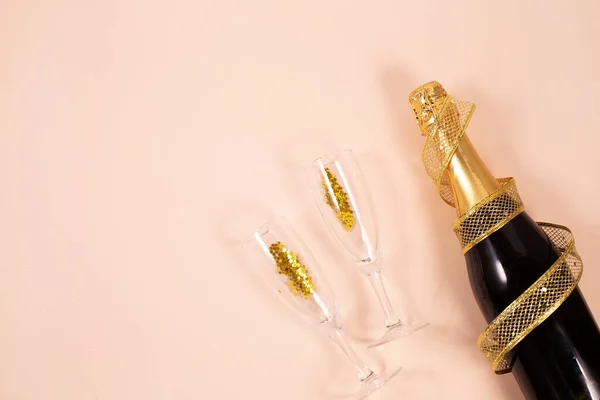 Butelka szampana ze szklankami, złotymi wstążkami i konfetti na jasnym tle — Zdjęcie stockowe
