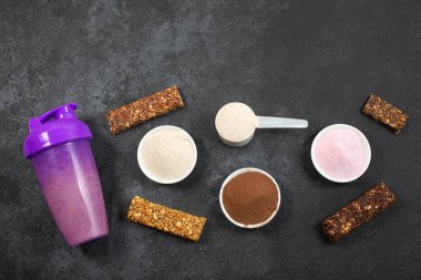 Titretici, kepçe dolusu protein tozu ve koyu arkaplanda enerji dolu musli çubukları ölçmek..
