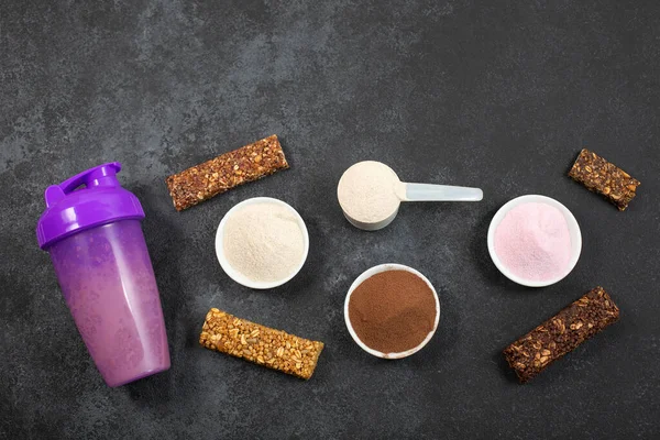 Titretici, kepçe dolusu protein tozu ve koyu arkaplanda enerji dolu musli çubukları ölçmek..